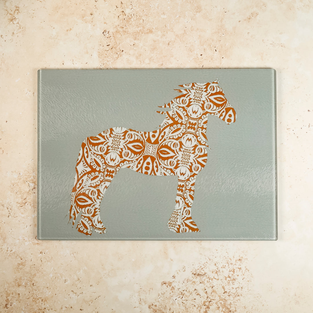 A grey glass worktop protector with a brown horse design on it, placed on a marble surface.