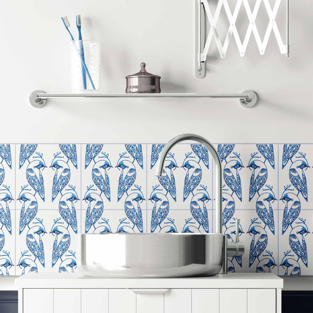 Bathroom with blue and white bird pattern on tiles, silver faucet, and white cabinets.