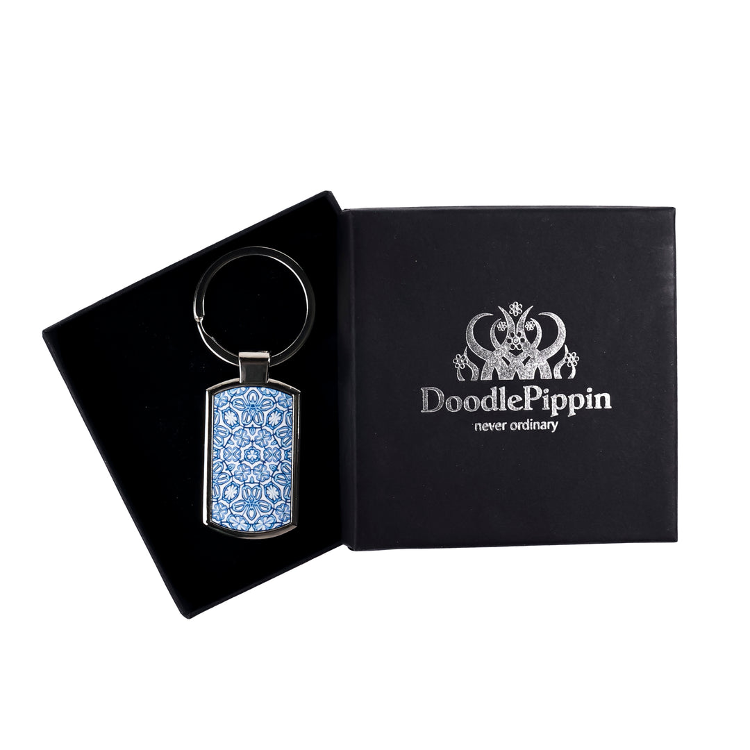 A metal keyring with a blue Turkish flower design, presented in a silver-embossed black DoodlePippin box with velvet liner.